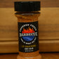 A bottle of Cooked Creek Barbecue dry rub seasoning on a wooden surface with a wooden background.