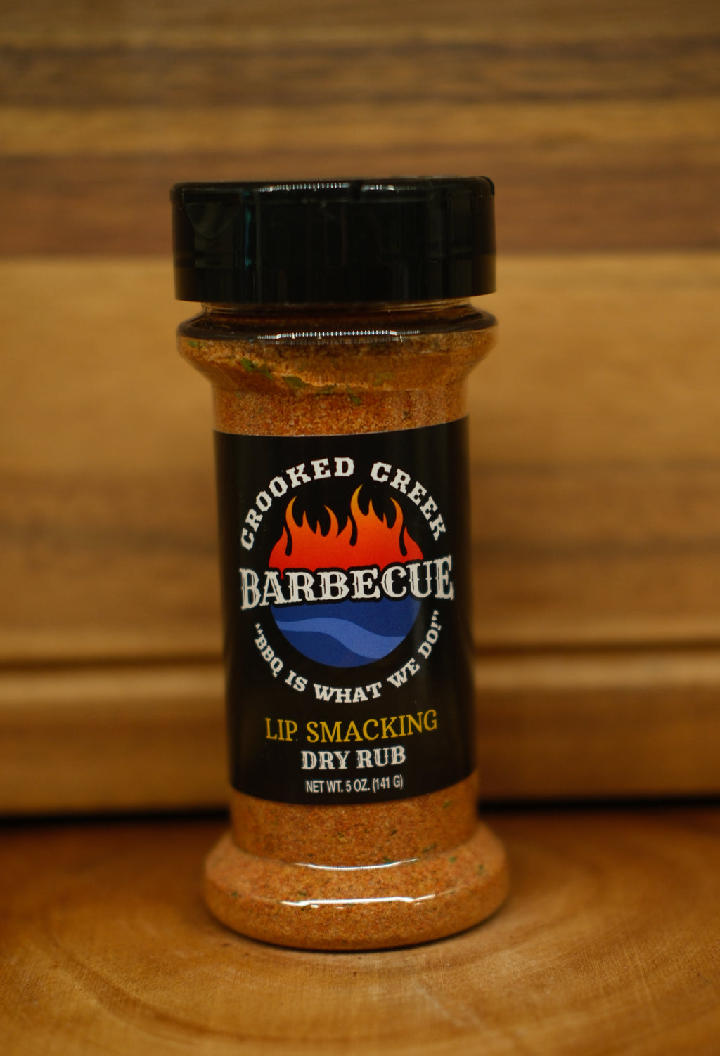 A bottle of Cooked Creek Barbecue dry rub seasoning on a wooden surface with a wooden background.