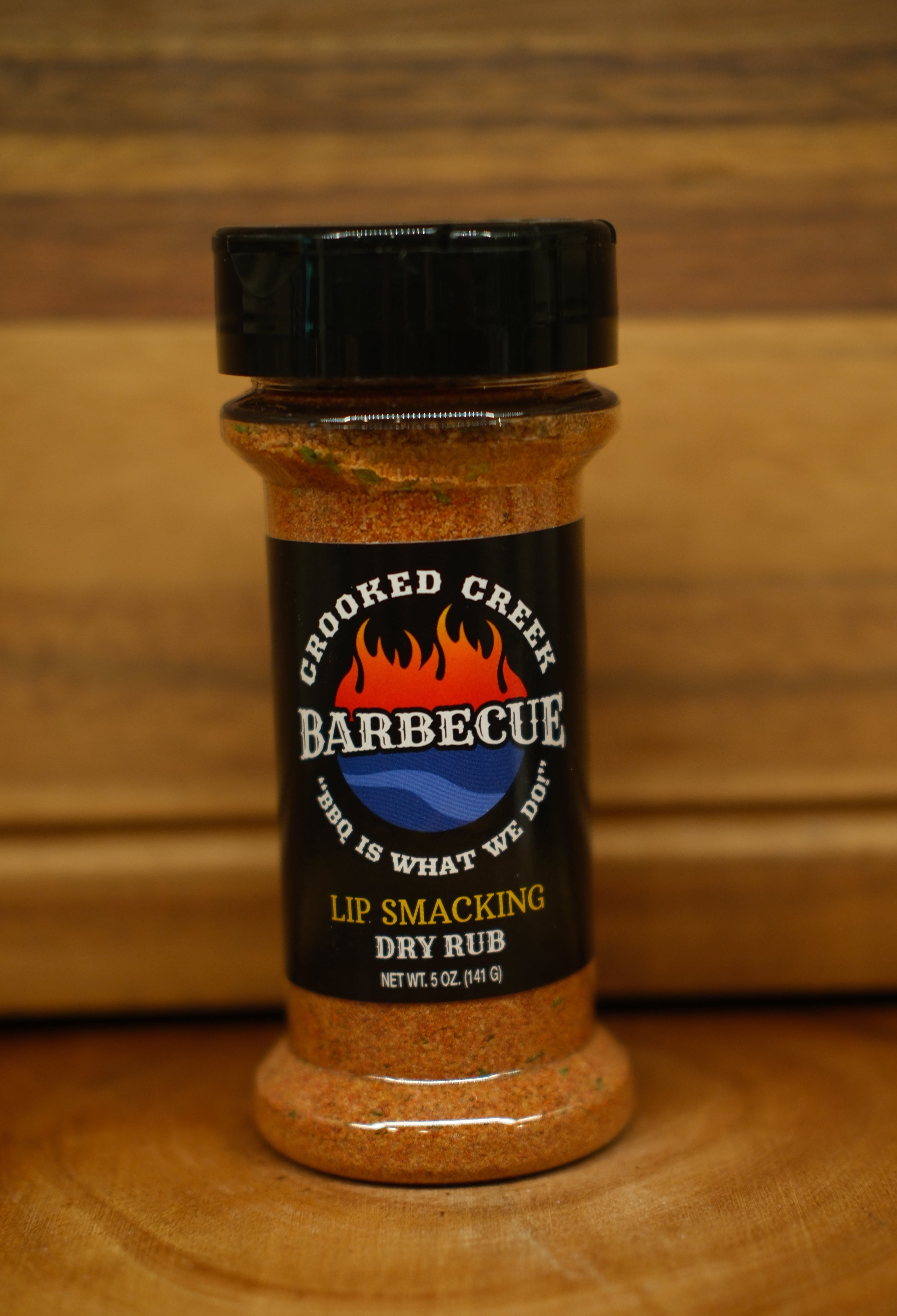 A bottle of Cooked Creek Barbecue dry rub seasoning on a wooden surface with a wooden background.